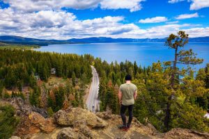 Featured image showing a man looking at Lake Tahoe from Eagle Rock in California, with Sierra Nevada Mountains in the background.